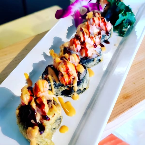 Yanagi Sushi's deep-fried sushi rolls topped with shrimp, orange and brown sauces, and a purple orchid.