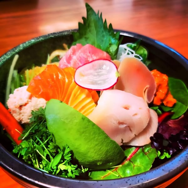 A vibrant Yanagi Sushi chirashi bowl with various fish, avocado, radish, and greens.